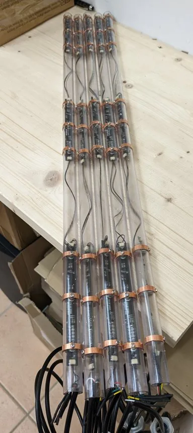 Fünf gleiche Bodenspieße liegen nebeneinander auf einer Werkbank, noch offen: Im durchsichtigen Kunststoffrohr steckt eine schmale Platine mit kupferfarbenen Ringen in gleichmäßigem Abstand, am unteren Ende tritt jeweils ein graues Anschlusskabel aus