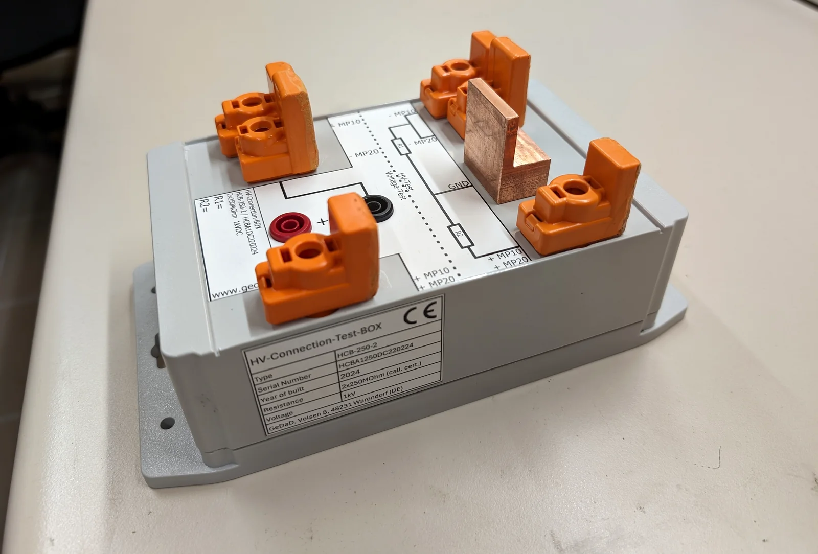 Anschlussbox HCB-250-2 im weißen Gehäuse, oben vier orangefarbene Anschlussklemmen, eine Kupferschiene und zwei Messbuchsen neben dem aufgedruckten Schaltbild, an der Stirnseite das Typenschild von GeDaD mit 2 × 250 Megaohm und 1 Kilovolt
